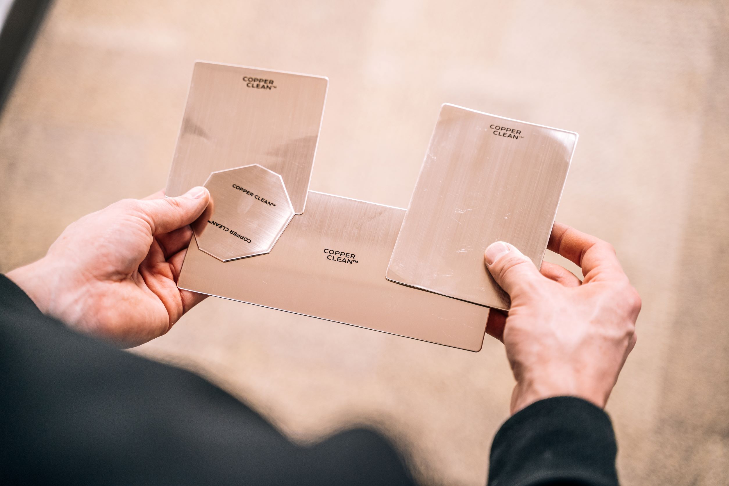A person holds four small copper patches of different sizes and shapes, which can be wrapped around or stuck to door handles.