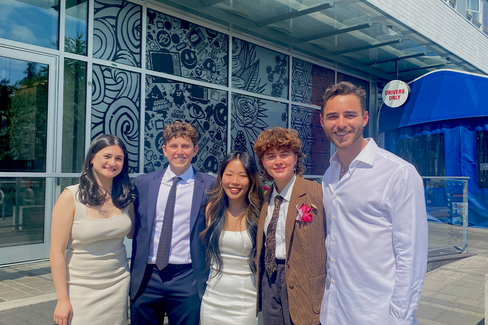 Group of 5 students smiling outside a restaurant on University Blvd.