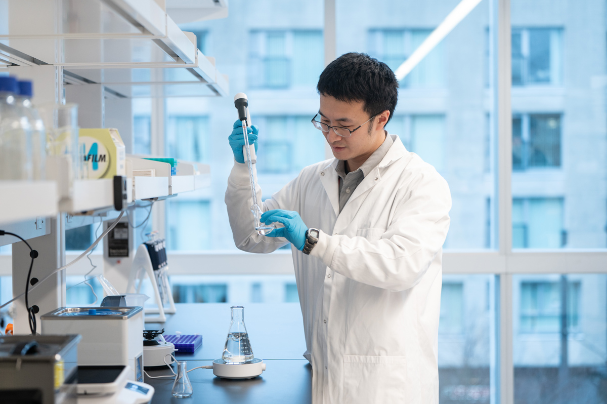 A student in a lab coat holding an Erlenmeyer flask