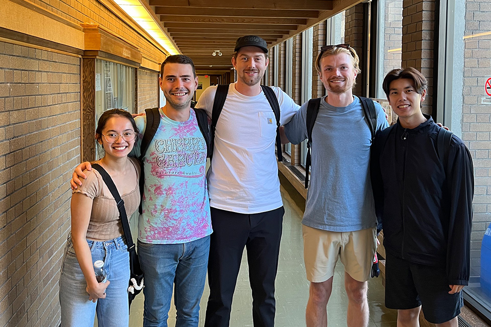 A group of 5 UBC students gathered in a hallway with a brick wall on the left
