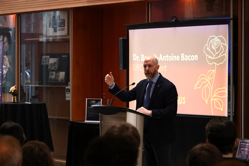 Dr. Benoit-Antoine Bacon speaks at a podium in front of a screen showing an illustration of a rose