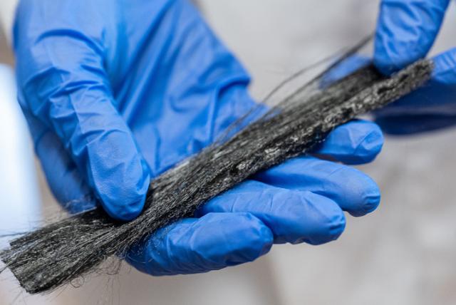 Researcher holding threads of black carbon fibres whilst wearing blue medical gloves