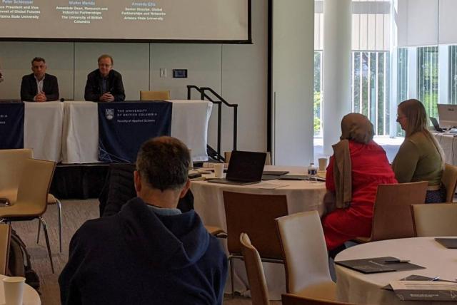 A panel of speakers is watched by guests at tables