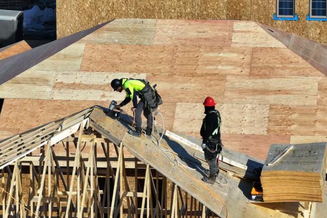 Two construction workers on top of a half-built wooden roof
