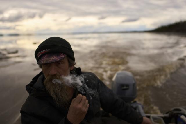 Jake Pogrebinsky smokes a cigarette while diving his boat on the Yukon River looking for logs to collect, Tuesday, May 20, 2025, in Galena, Alaska. (AP Photo/John Locher)