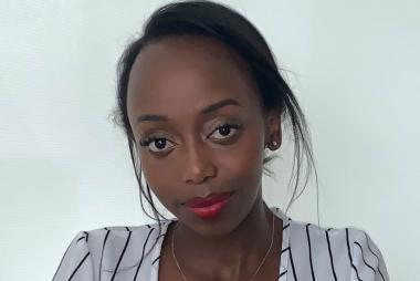 A headshot photo of Ashley Kairu, centered, as she softly smiles at the camera.