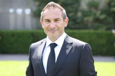 Headshot image of Dr. Davide Elmo from the chest up. He is wearing a suit jacket and tie while outside with green grass in the background.