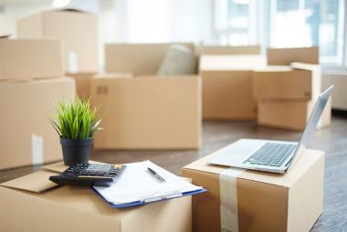 Cardboard boxes in empty house with a laptop on top of one of the boxes