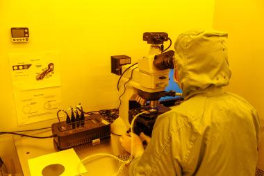 A person looking into a microscope in a room with yellow-hued light