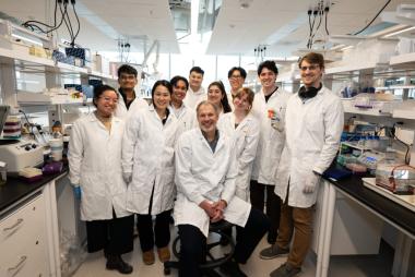 Dr. Peter Zandstra seated in a lab, surrounded by trainings, all wearing white lab coats. 