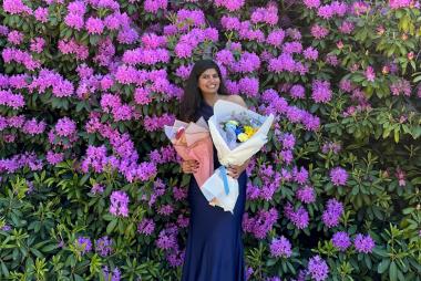 Ananya Swaminathan in front of flowering greenery, holding two bouquets of flowers