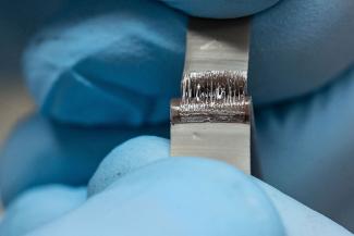 A close-up of hands dressed in blue latex gloves as they pull apart a test strip that showcases self-healing polymers separating and reforming