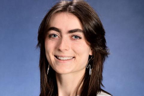 Lucy Myrol smiles for the camera, centered in front of a blue photo backdrop
