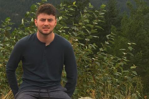 Nik Provenzano is seated outdoors in front of greenery while looking at the camera 