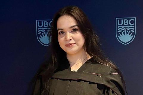 Mahjoba Shariq poses in her academic regalia in front of a UBC backdrop
